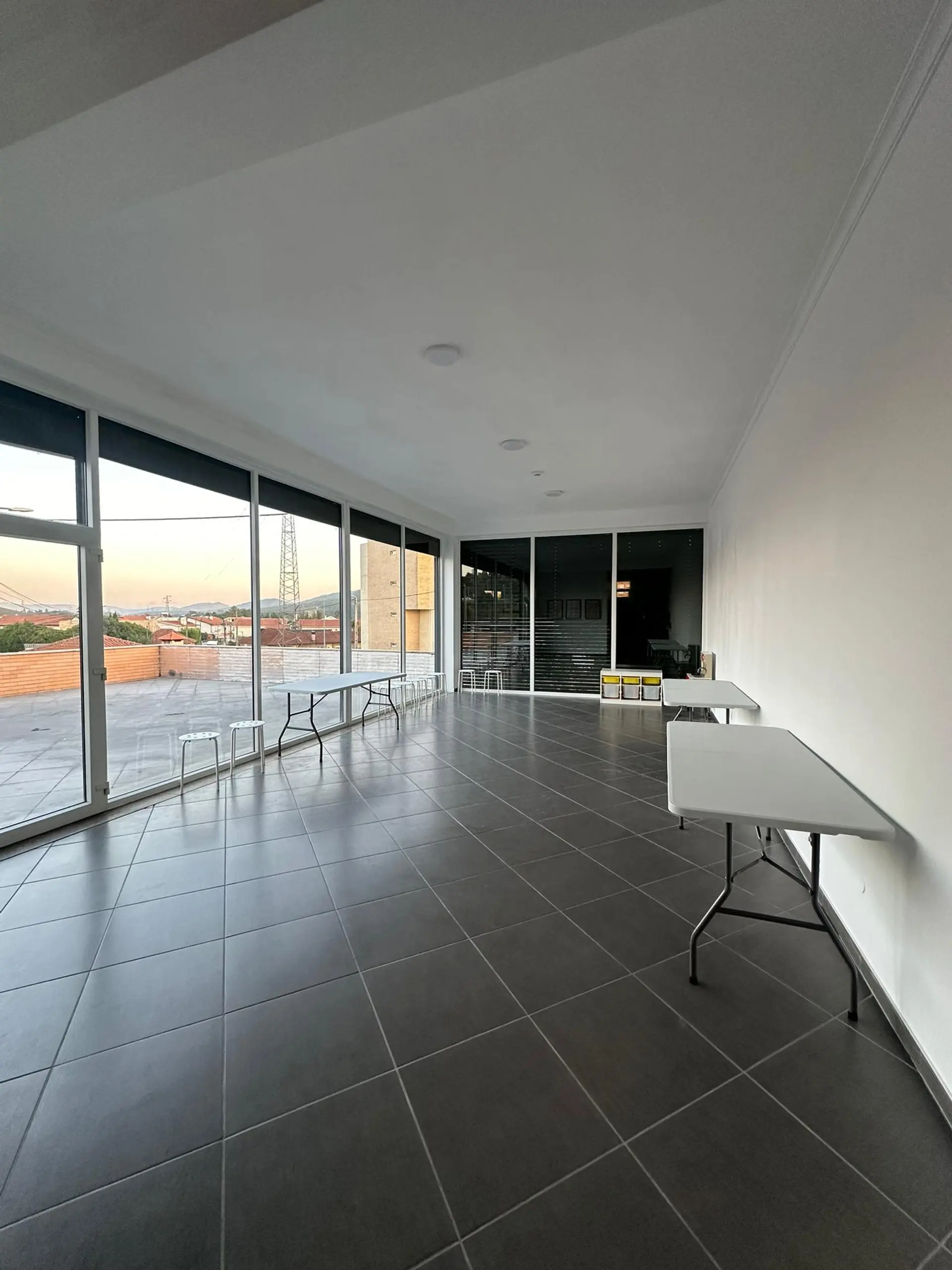 Sala ampla do espaço Mariadita, com paredes de vidro e vista sobre a cidade ao pôr do sol